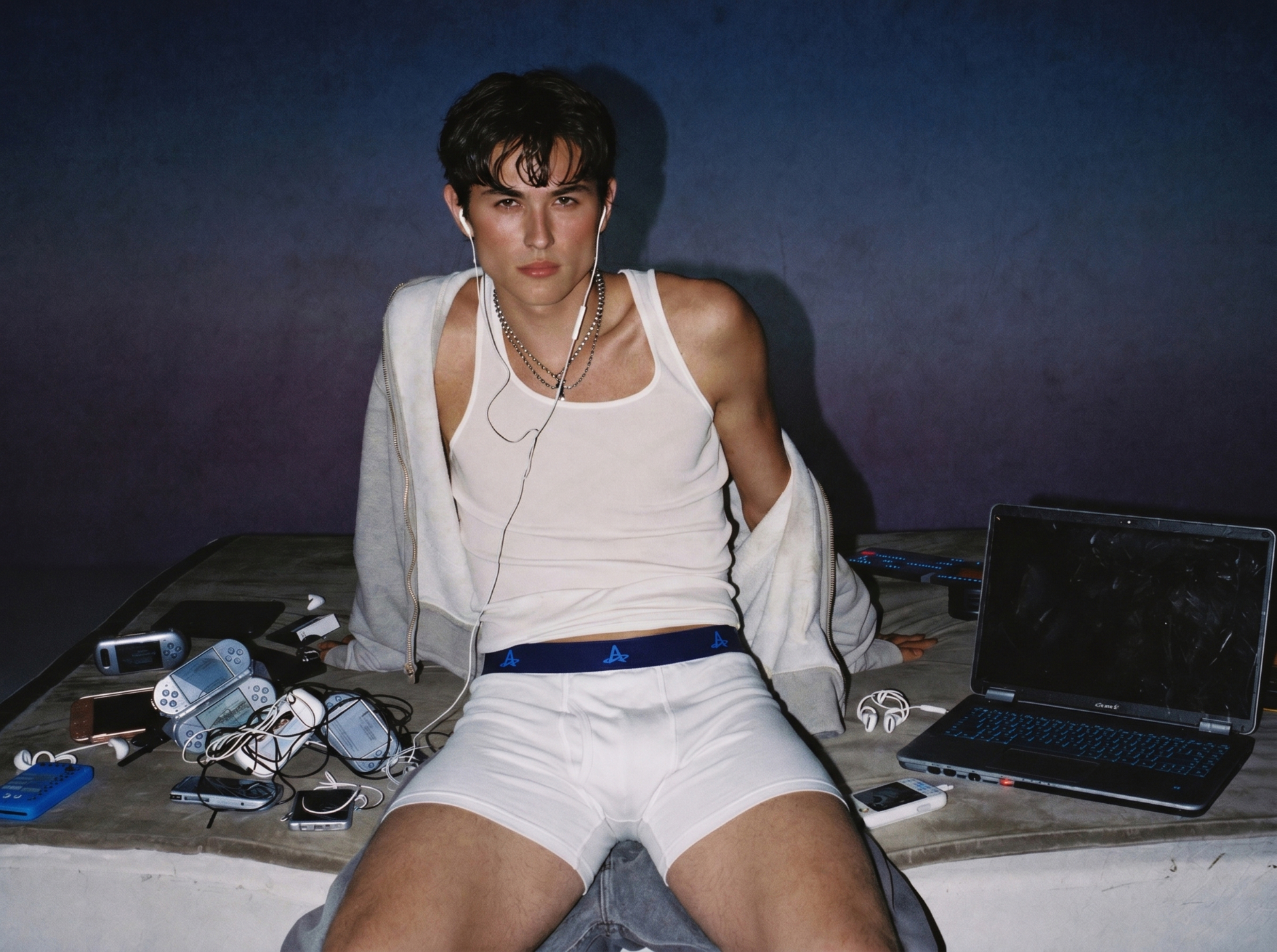 Male model seated on a table wearing white Action Replay boxer briefs surrounded by retro tech.