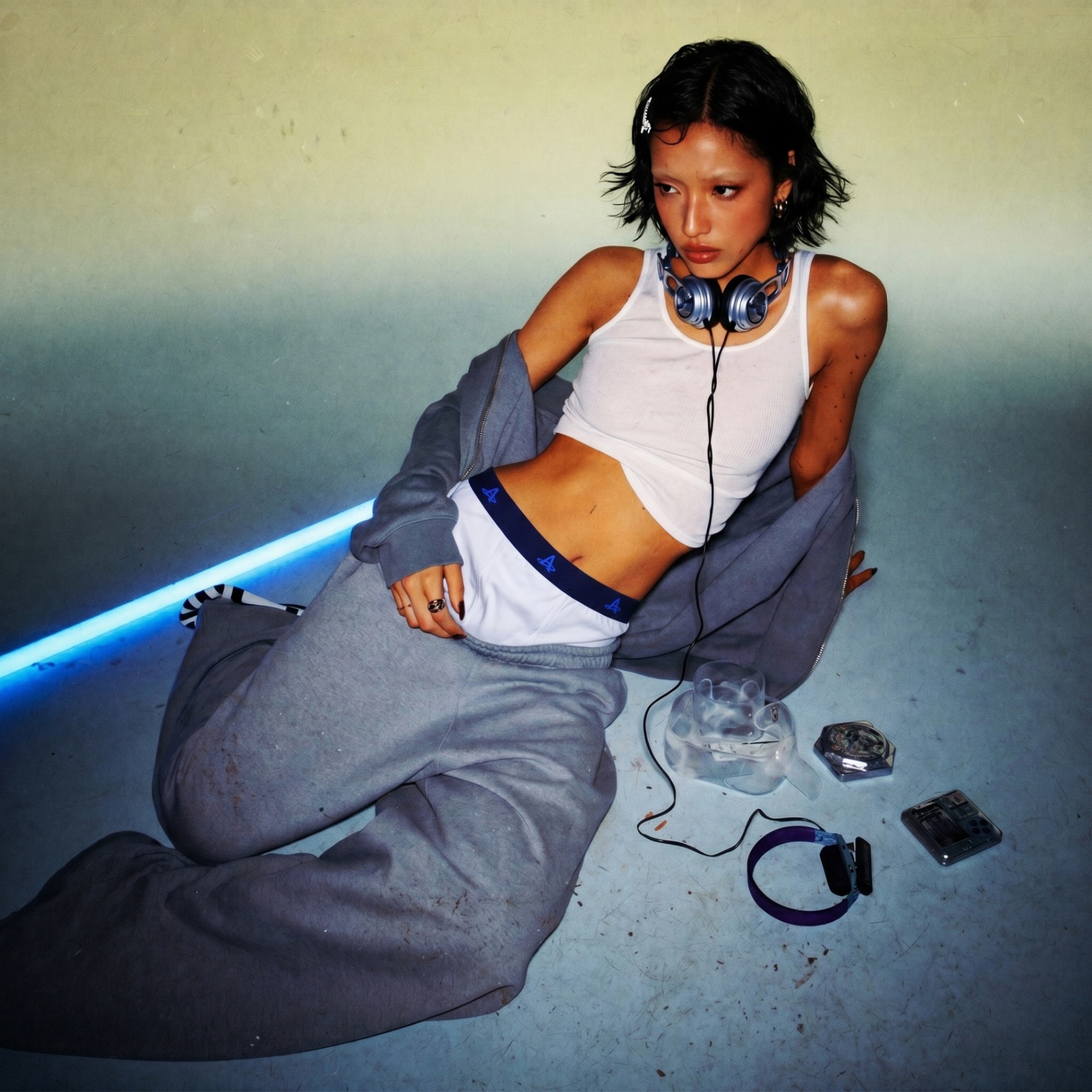 Model on a studio floor styled in white Action Replay boxers and a slate zip hoodie with wired headphones.